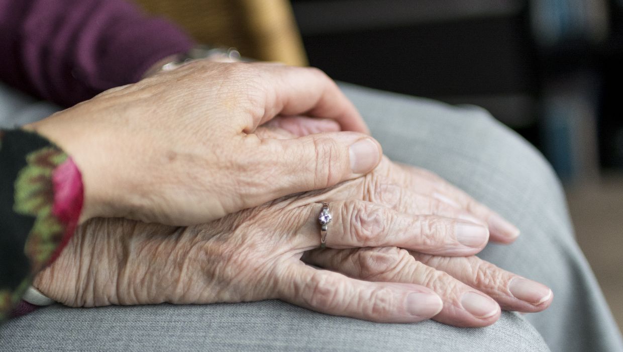 Person putting a hand on an elderly person's hand tile