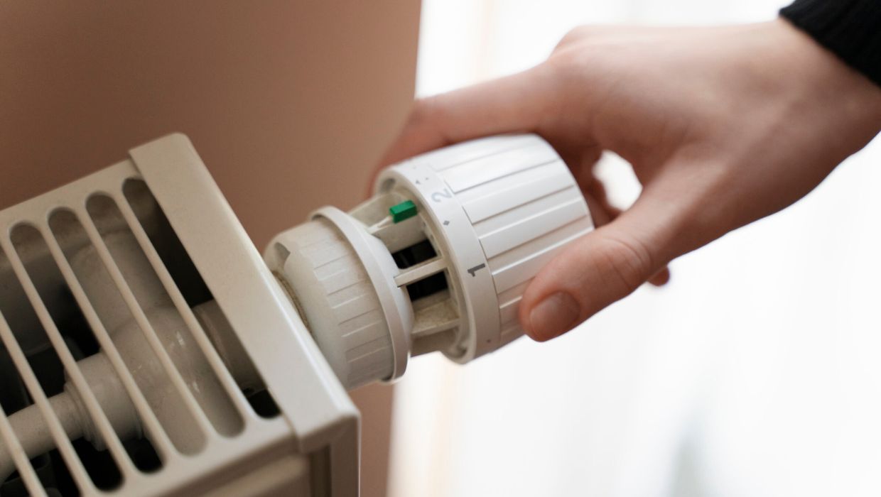 Person turning a thermostat on a radiator tile