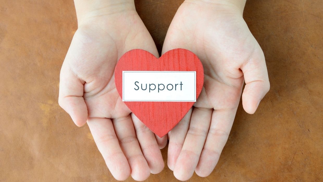 The word support on a cut out heart shape being held by a person