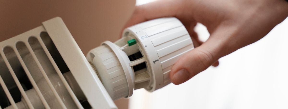 Person turning a thermostat on a radiator