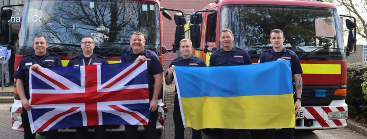 Two fire engines in the background with fire officers holding up the Union Jack and Ukrainian flags