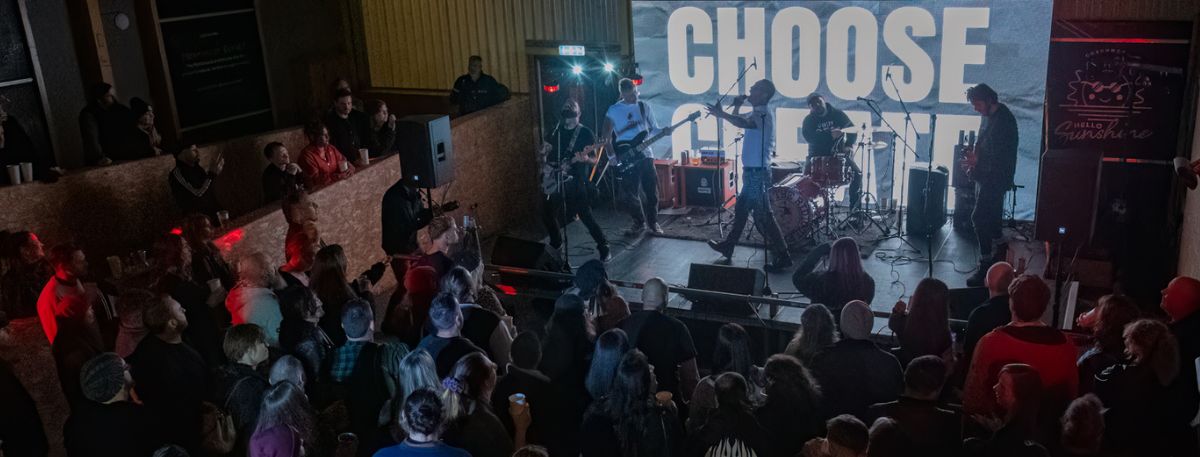 A man signing on stage with a sign in the background that has choose create written and people in the crowd