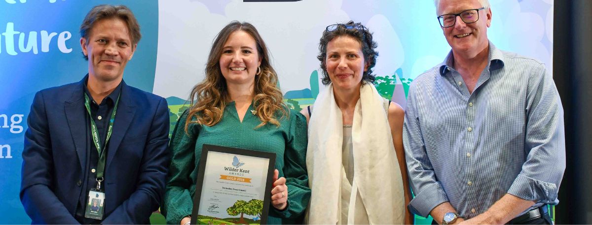 People standing in front of a blue backdrop that says 'Kent Wildlife Trust' and one person holding a certificate that says 'Gold Award' 