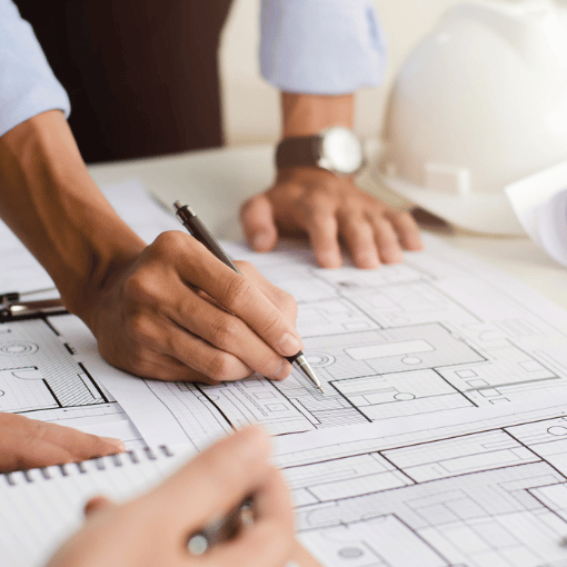 Image entitled image of mans hands drawing on building plans laid out on a table.